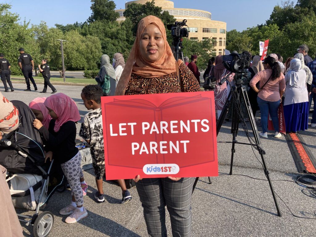 Black Muslim mom holds sign reading
